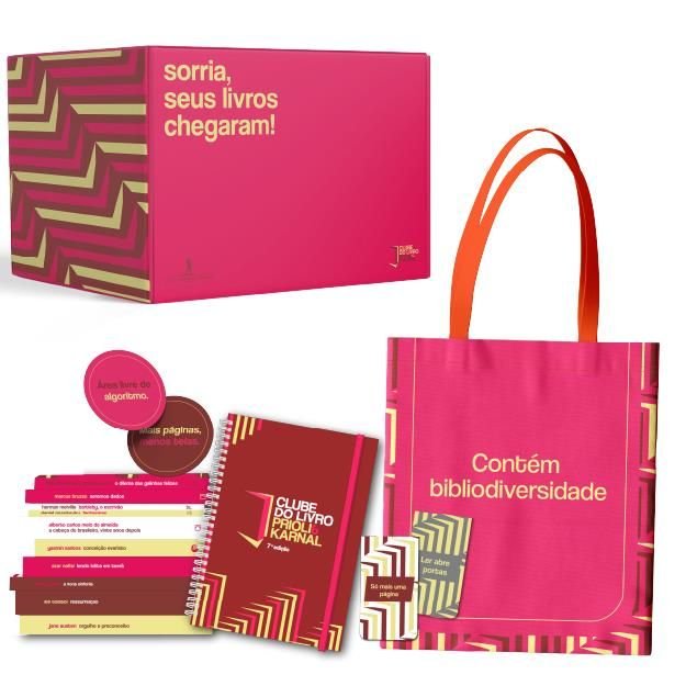 Flat‑lay da caixa do Box Clube do Livro 2026 aberta, exibindo 10 livros com sobrecapas exclusivas, um livro extra e 5 brindes premium (planner, ecobag, marcadores magnéticos, vela e xícara).